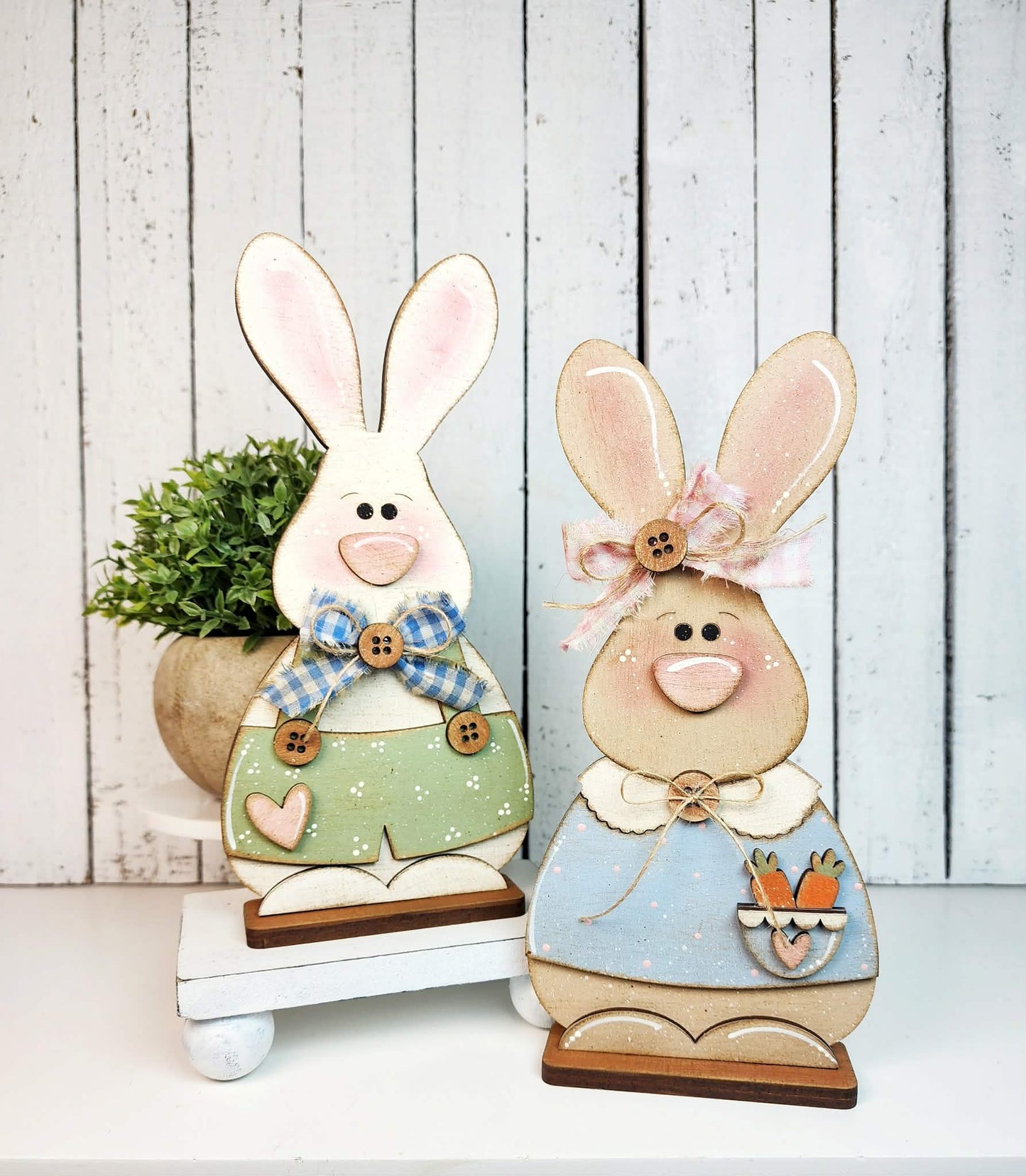 Two decorative bunny figures with pastel colors and cute details on a wooden surface.