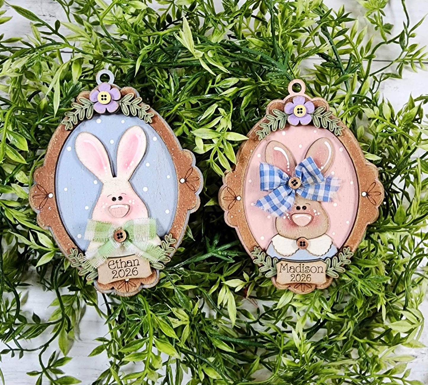 Two decorative Easter bunny ornaments with personalized names on a green leafy background.