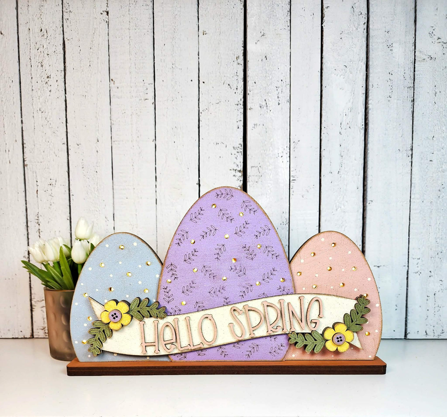 Decorative sign with colorful Easter eggs and 'Hello Spring' text against a wooden background.